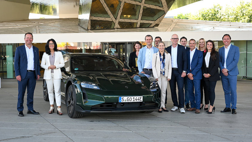 a group of people posing for a photo next to a car a group of people posing for a photo next to a car