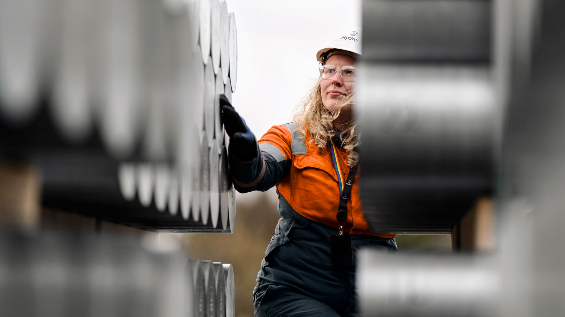 a woman wearing a hard hat and safety vest touching a stack of metal cylinders